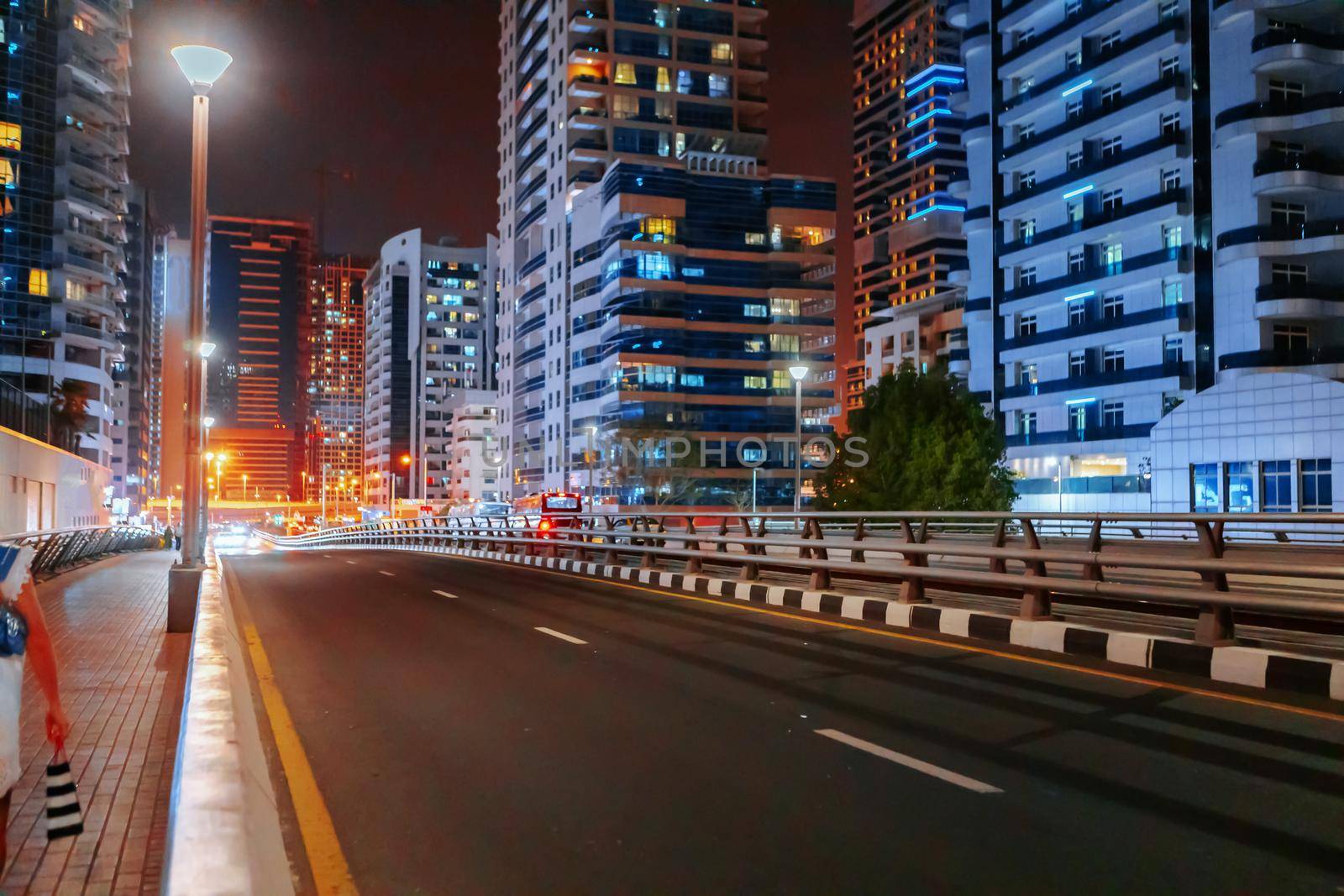 Empty asphalt road with modern buildings at night in Dubai, UAE