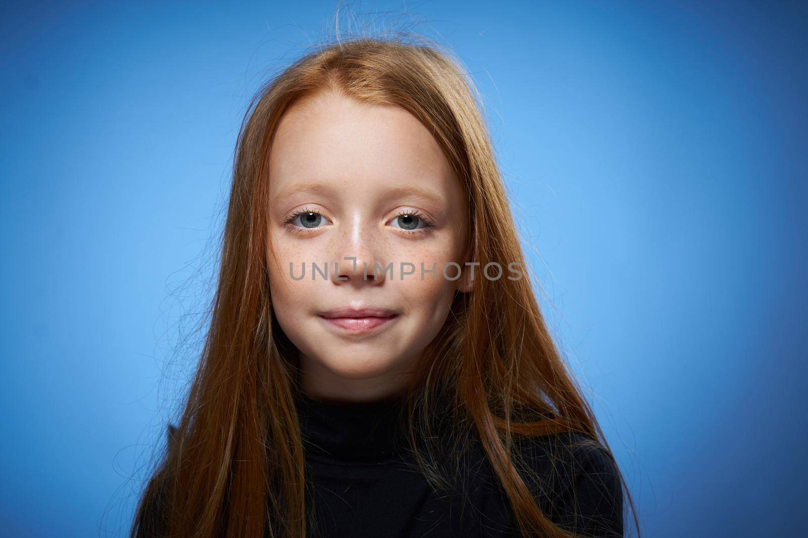 redhead girl with freckles on her face posing close-up blue background. High quality photo