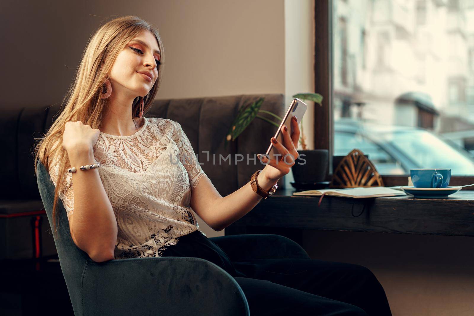 Happy young woman using her smartphone while sitting in cafeteria. Close up.