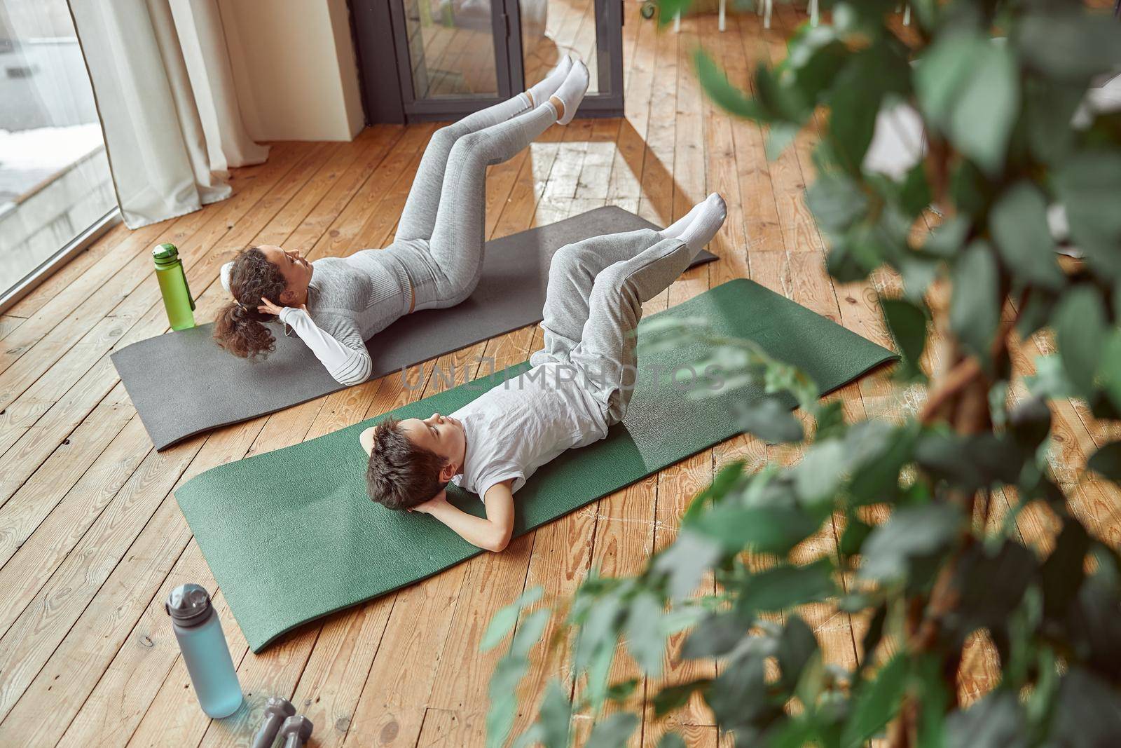 Top view of sporty female and boy doing crunches on mat during training together at home