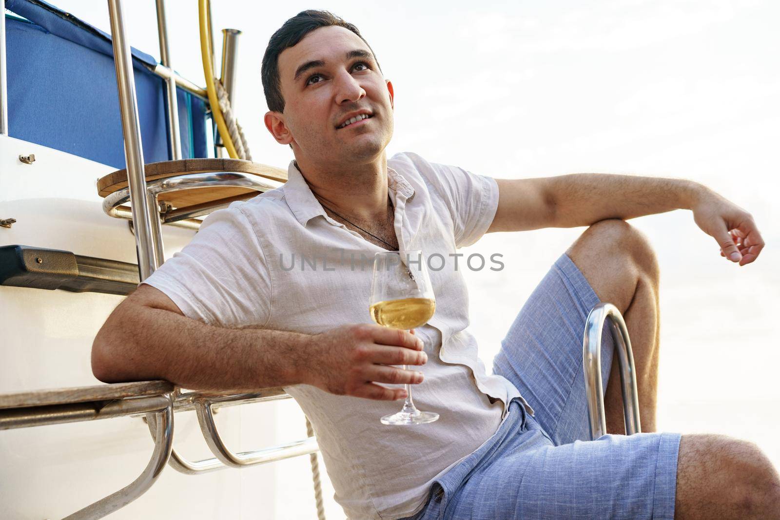 Young man holding a glass of wine on an open deck of a cruise boat, close up