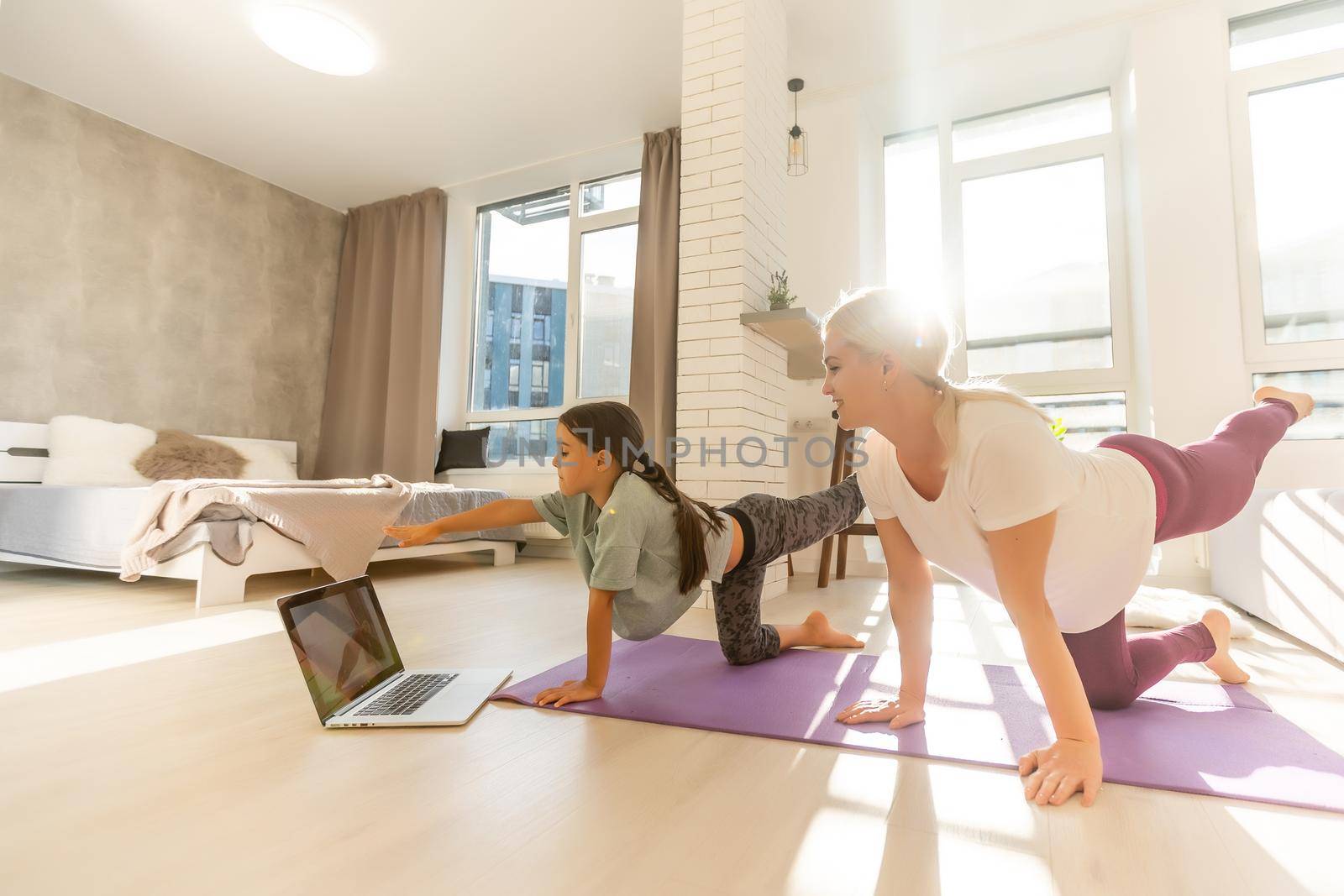 Young adult mother with her daughter watching online training together at home, looking a laptop