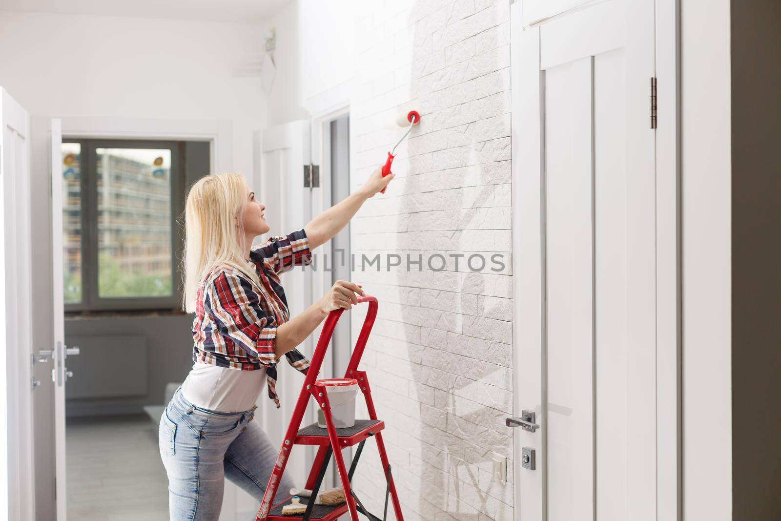 Beautiful young woman painting wall in room