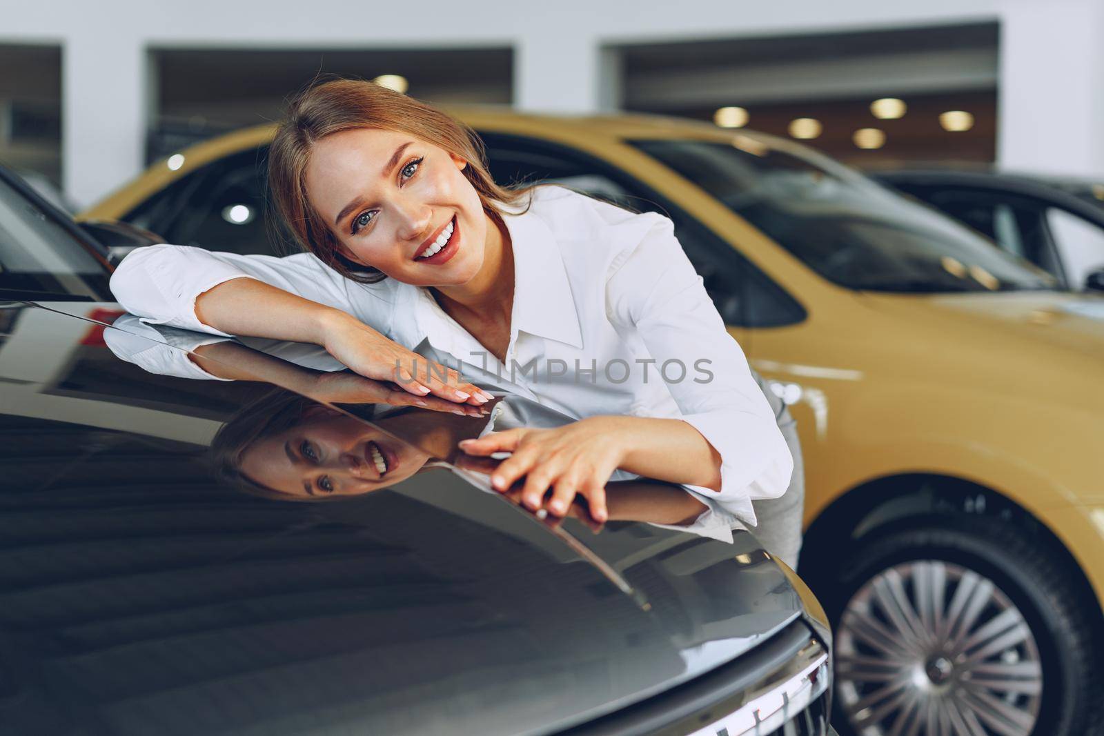 Beautiful young woman touching her new car with pleasure and joy