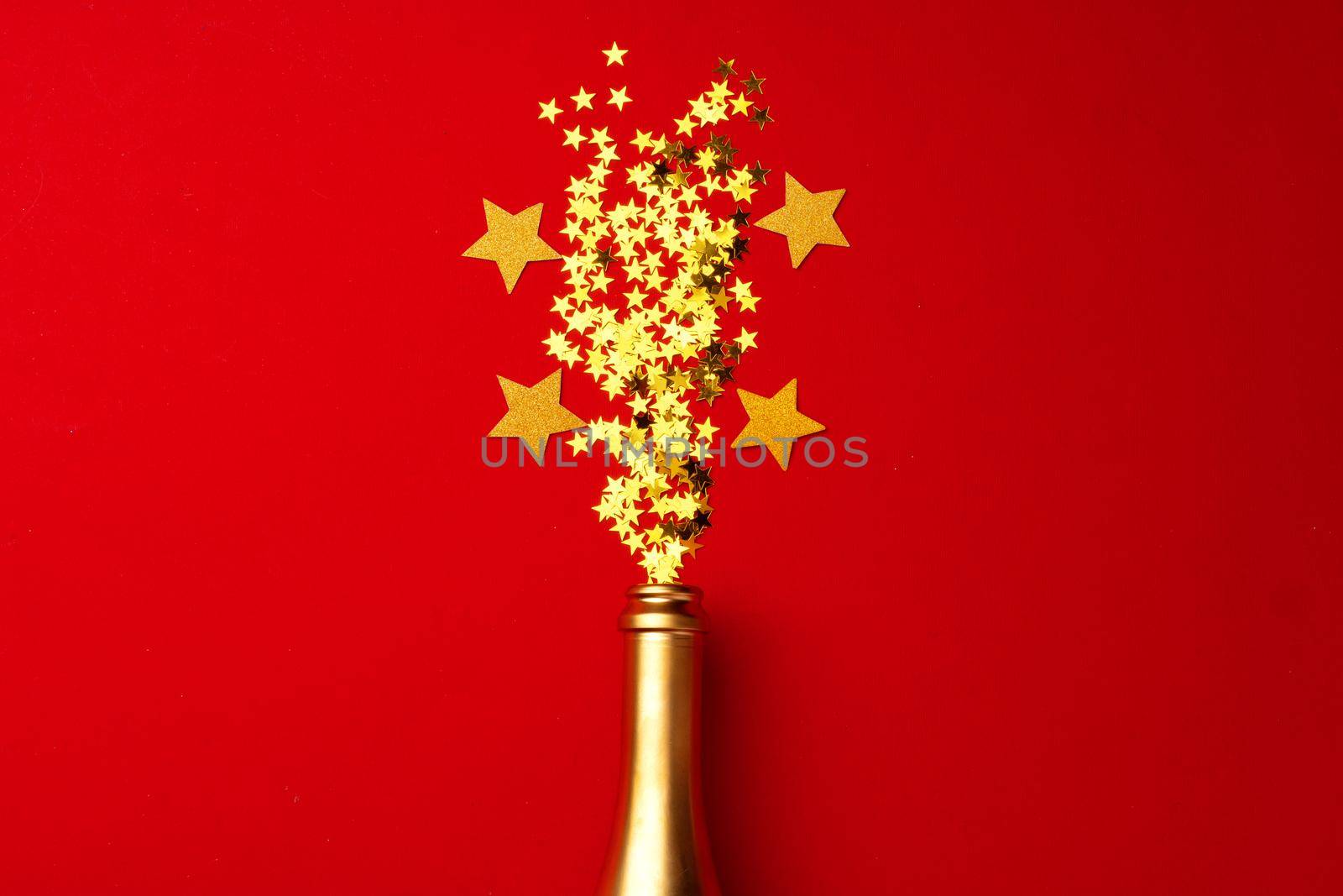 Champagne bottle with sparkling confetti on red background flat lay top view