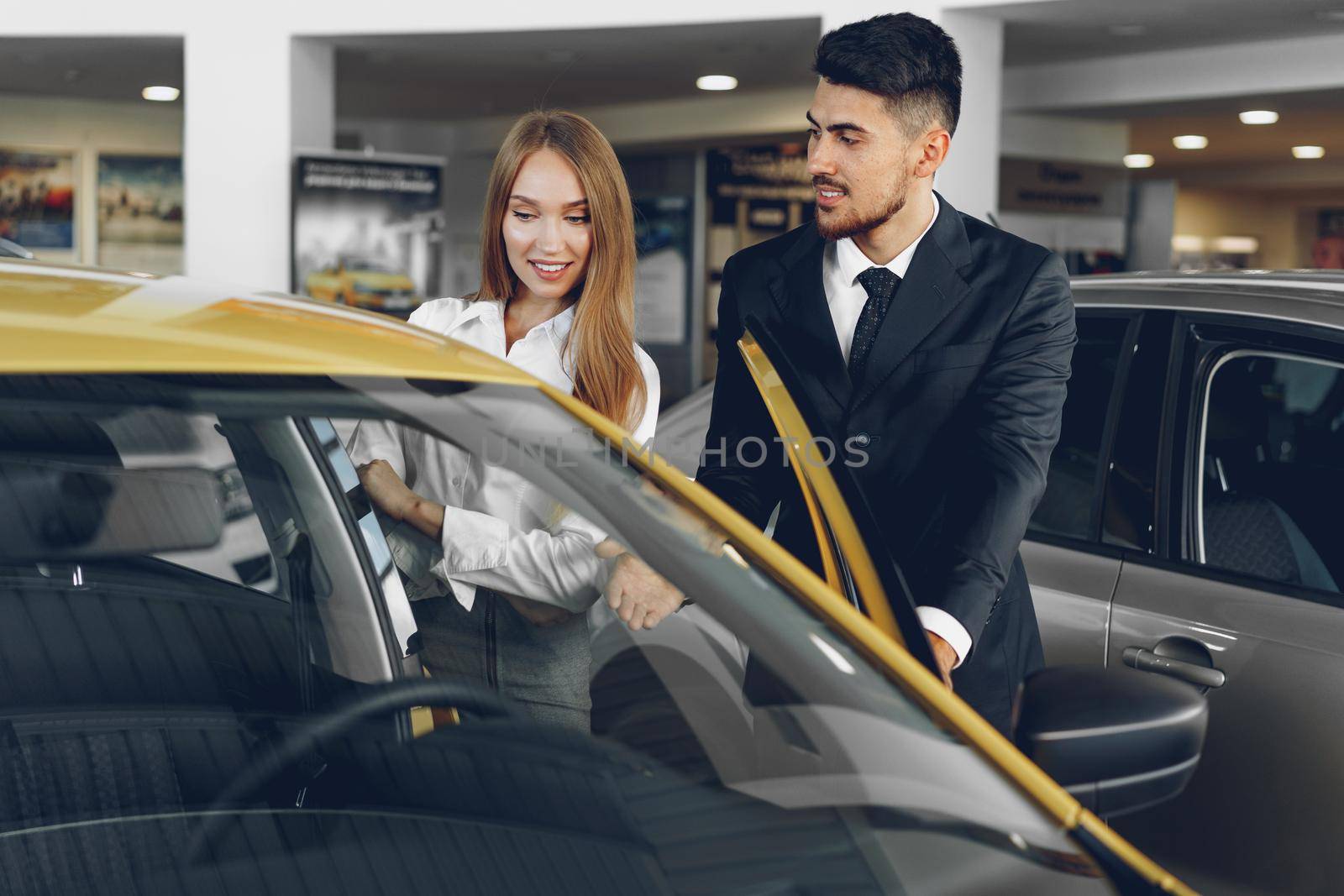 Man car dealer showing a woman buyer a new car in car salon