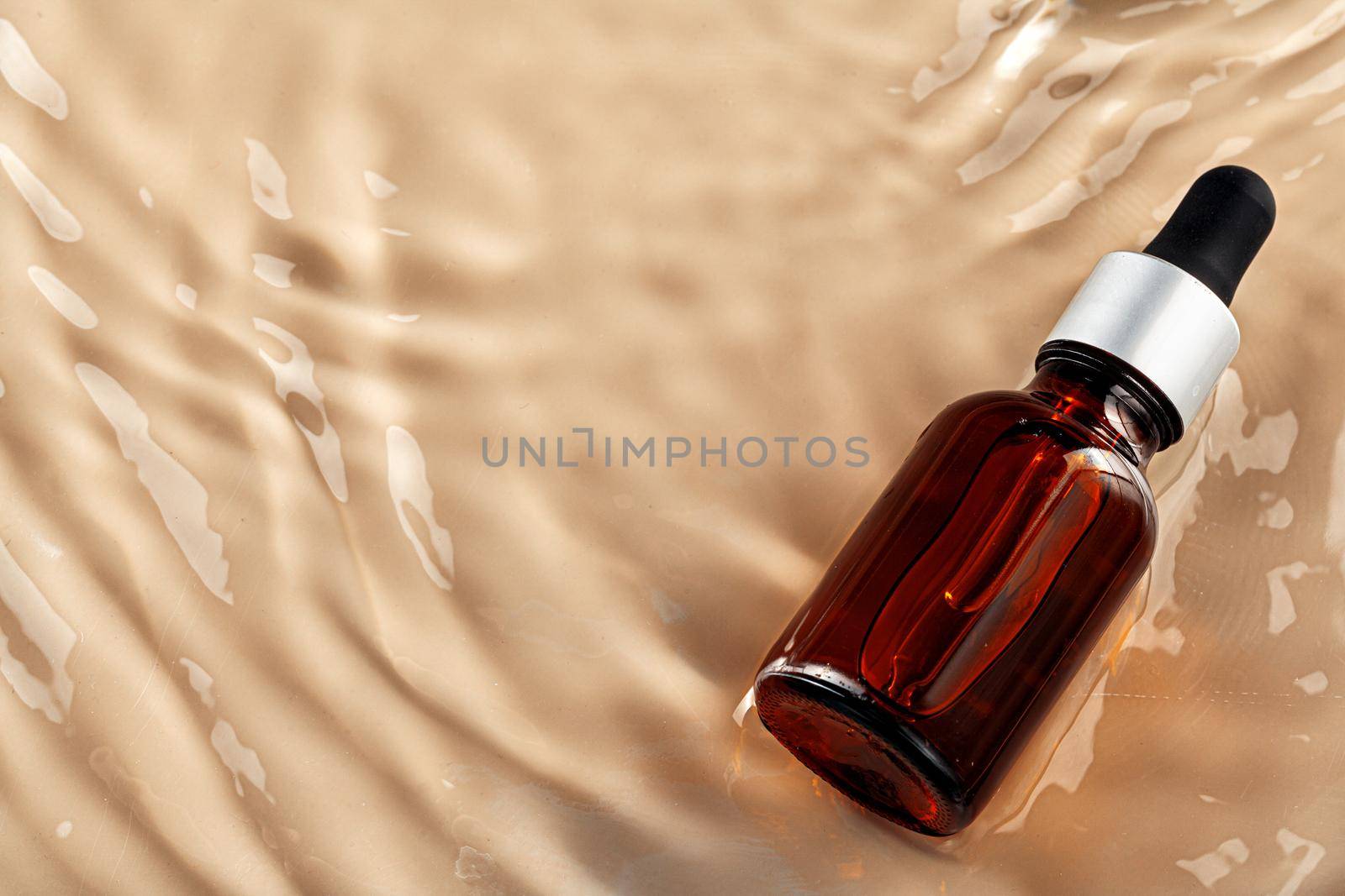 Cosmetic bottle with pipette in wavy water, top view