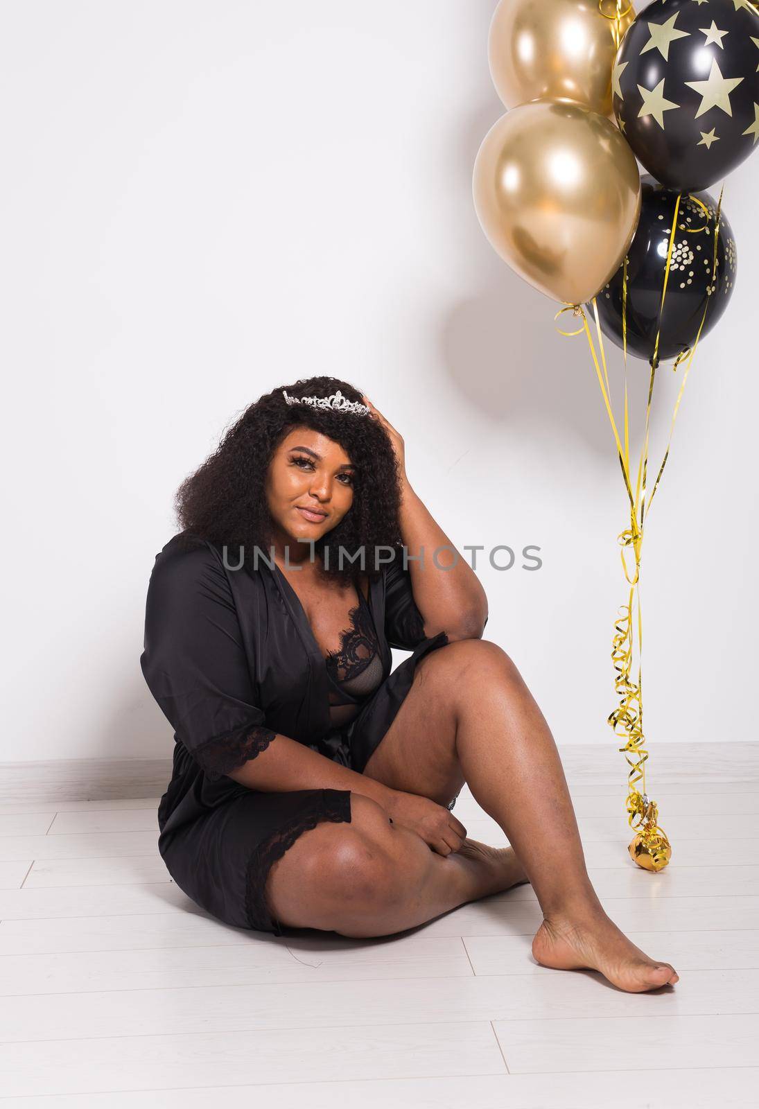 Portrait of smiling young African-American adult woman looking sweet on yellow background holding balloons.