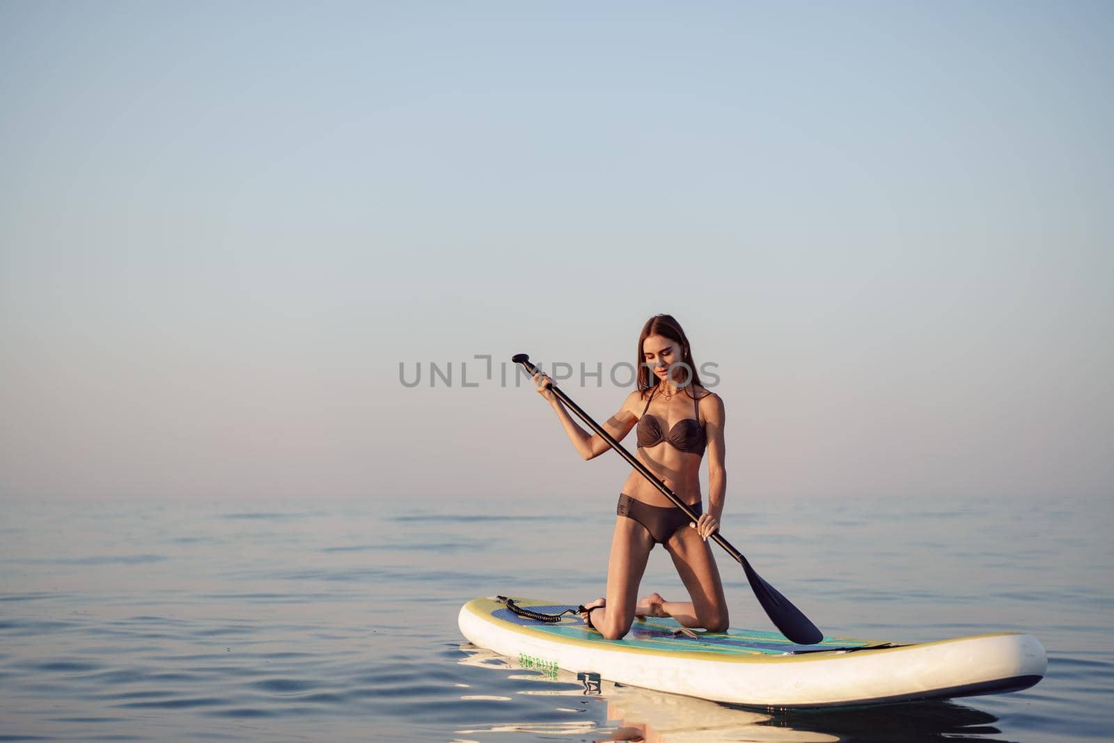 Young attractive woman standing on paddle board at sunrise