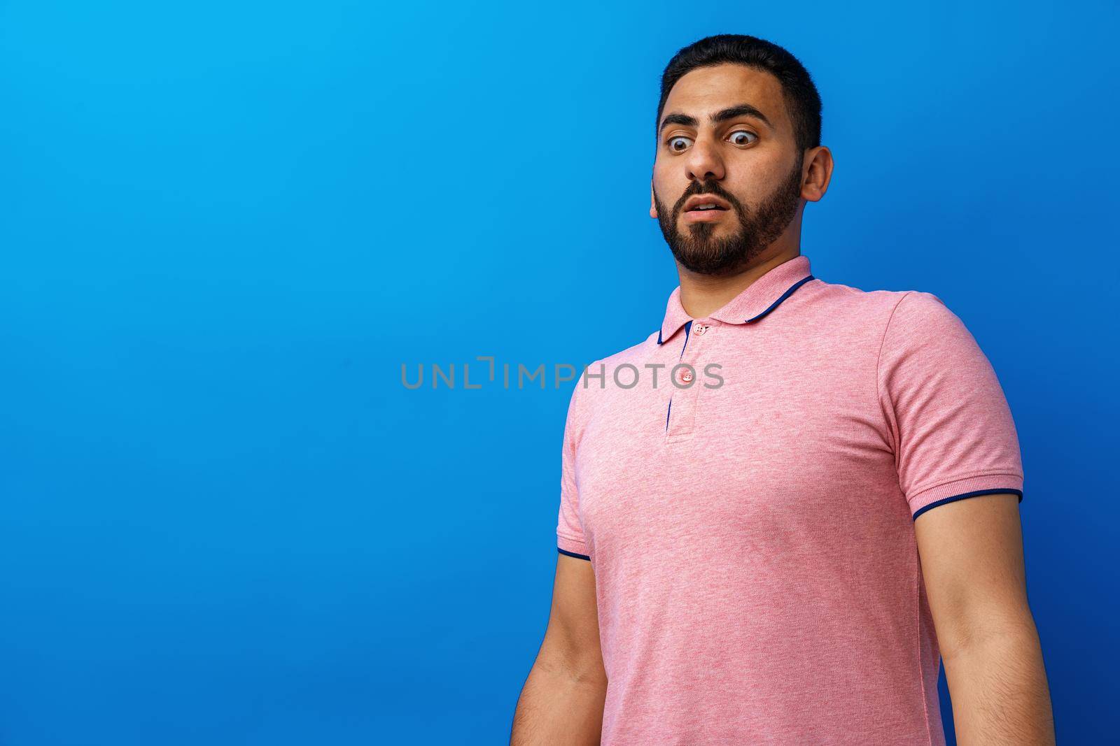 Young man nervous and scared looking at something against blue background, close up