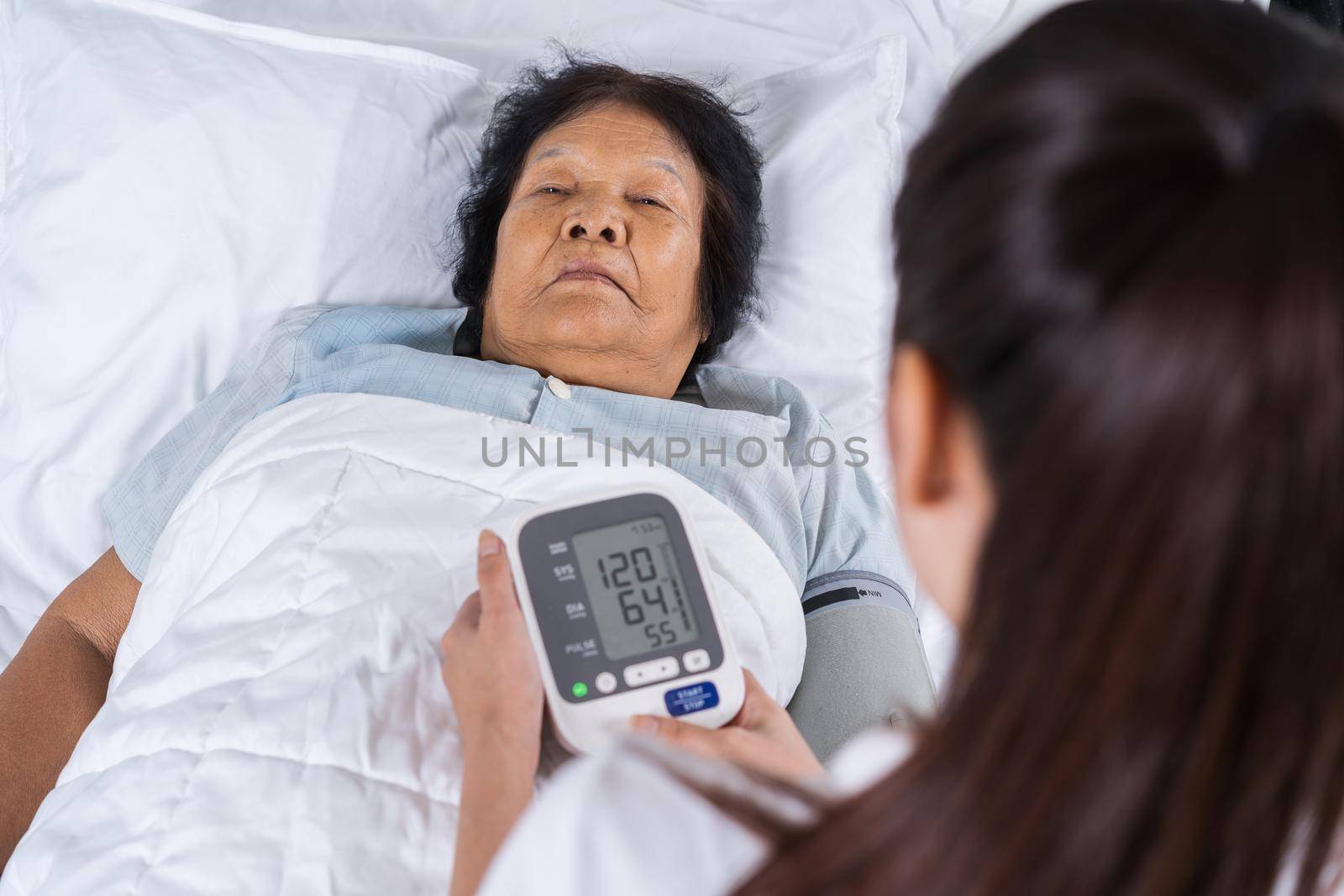 nurse checking blood pressure of a senior woman on bed by geargodz