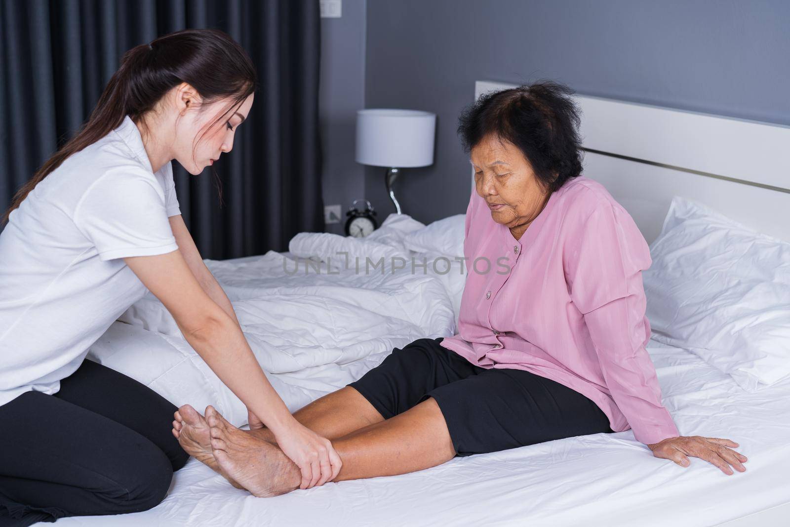 woman hands doing massage on old woman pain legs in a bed