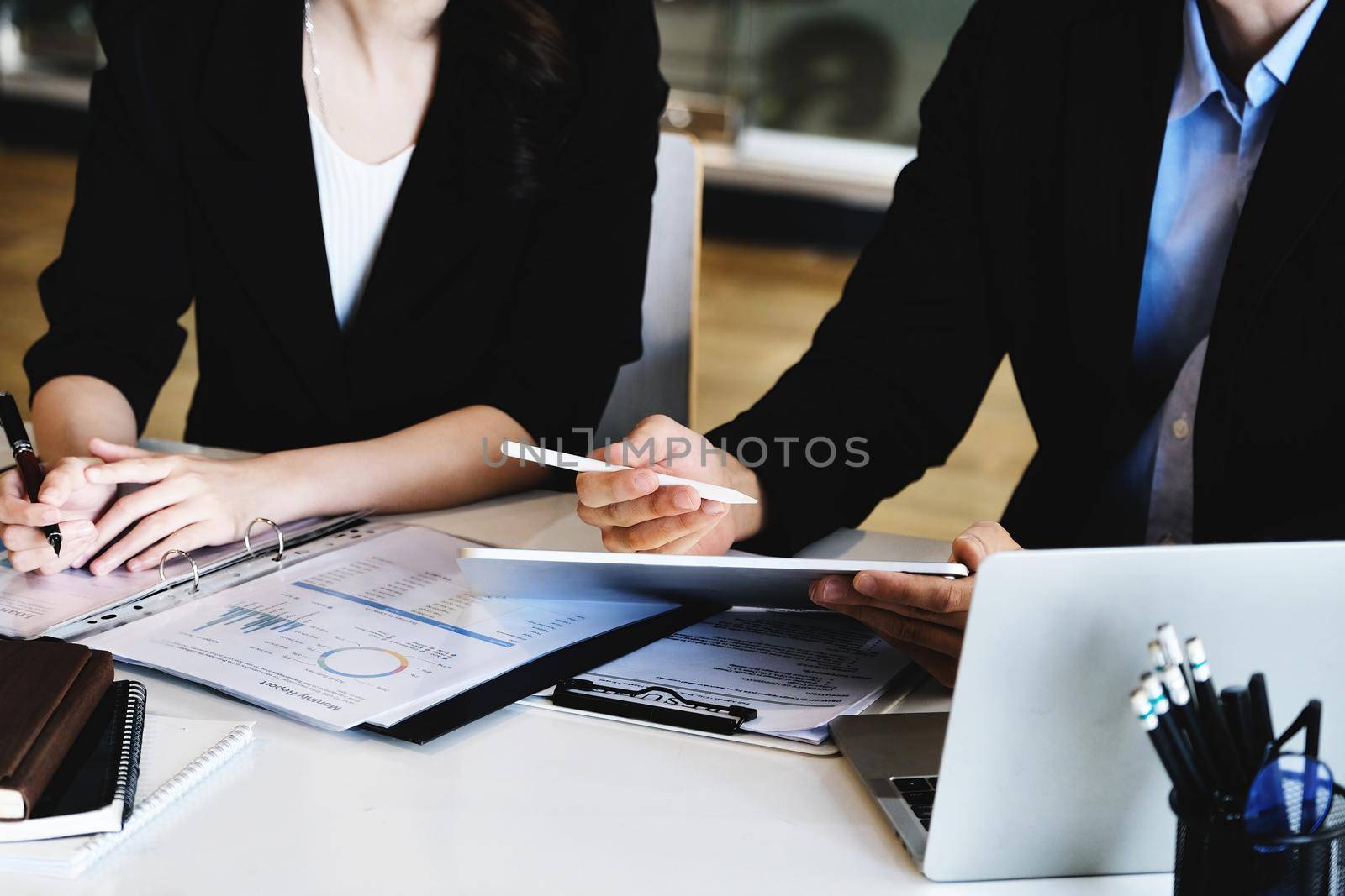 At the consultation, a male adviser uses a pen to point at a tablet to explain the profit restructuring to female business owners. by Manastrong