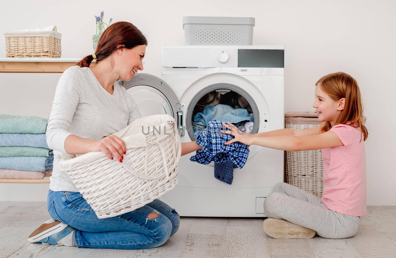 Happy mother and little daughter washing clothes using machine in light room
