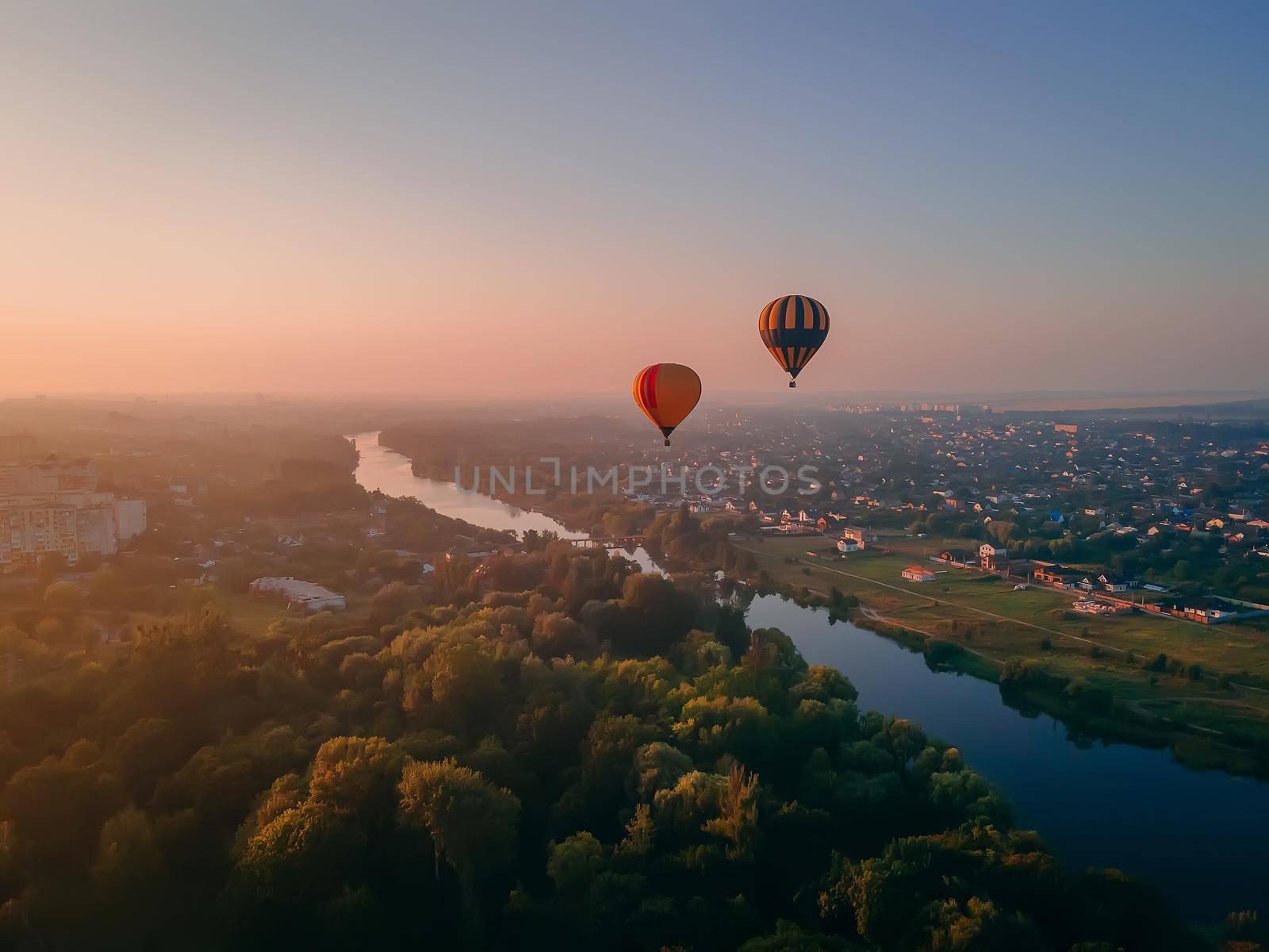 Two colorful air balloons flying over green park and river in small european city at summer sunrise, Kiev region, Ukraine