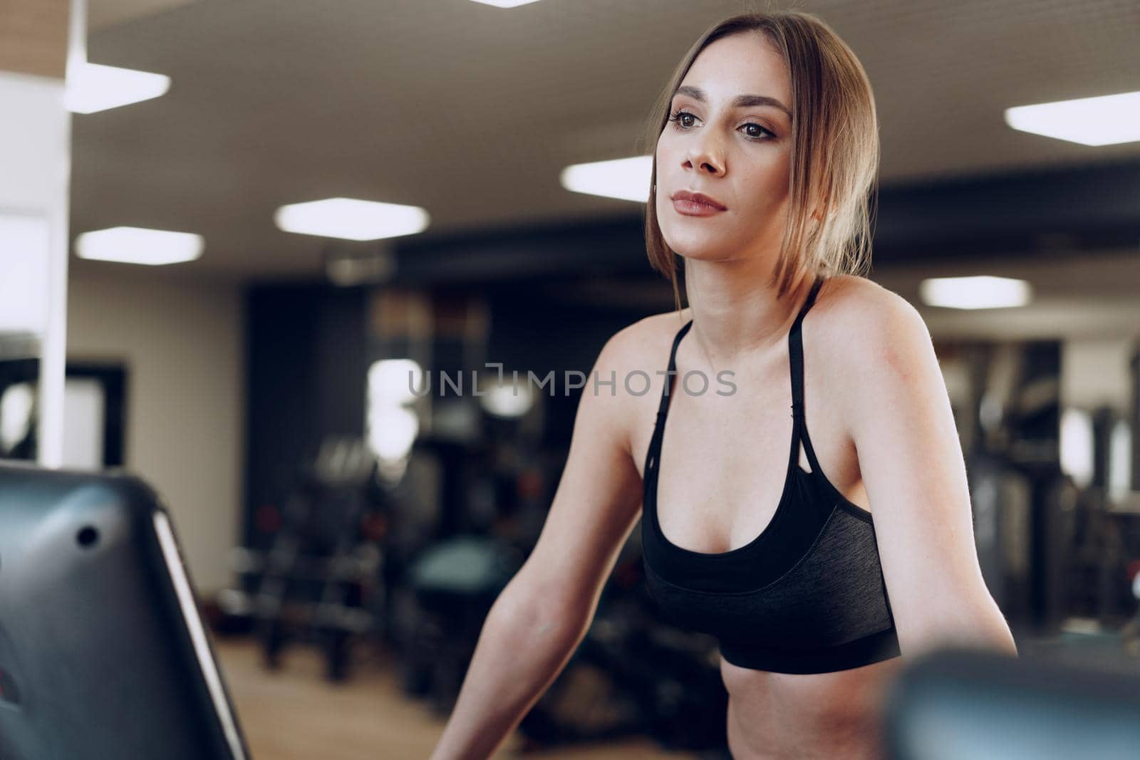 Pretty fit woman in black sportrswear training on a treadmill in fitness club