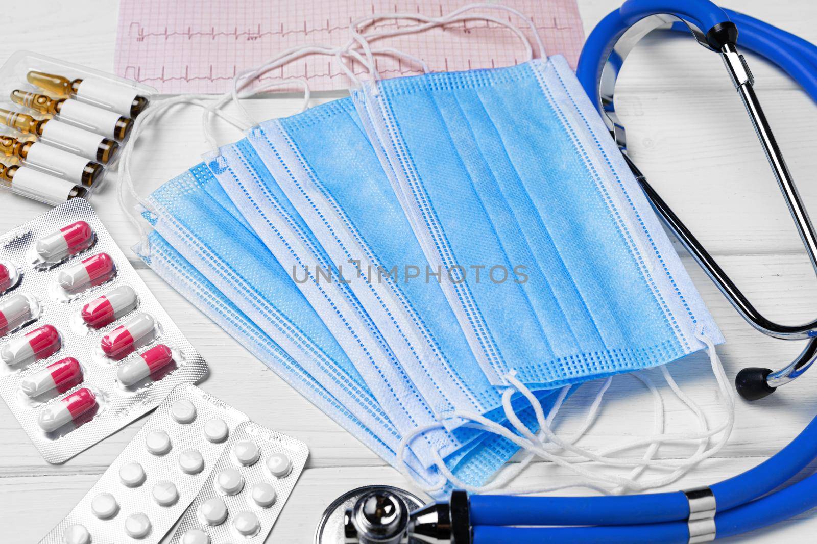 Medical equipment. Stethoscope, mask and pills on white wooden desk close up