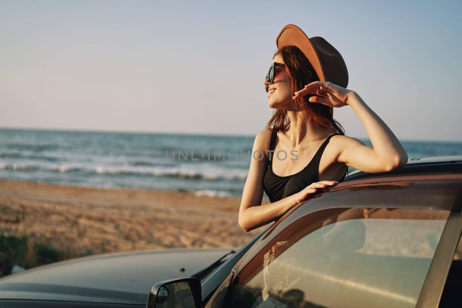 cheerful woman in sunglasses and a hat on the ocean near the car. High quality photo