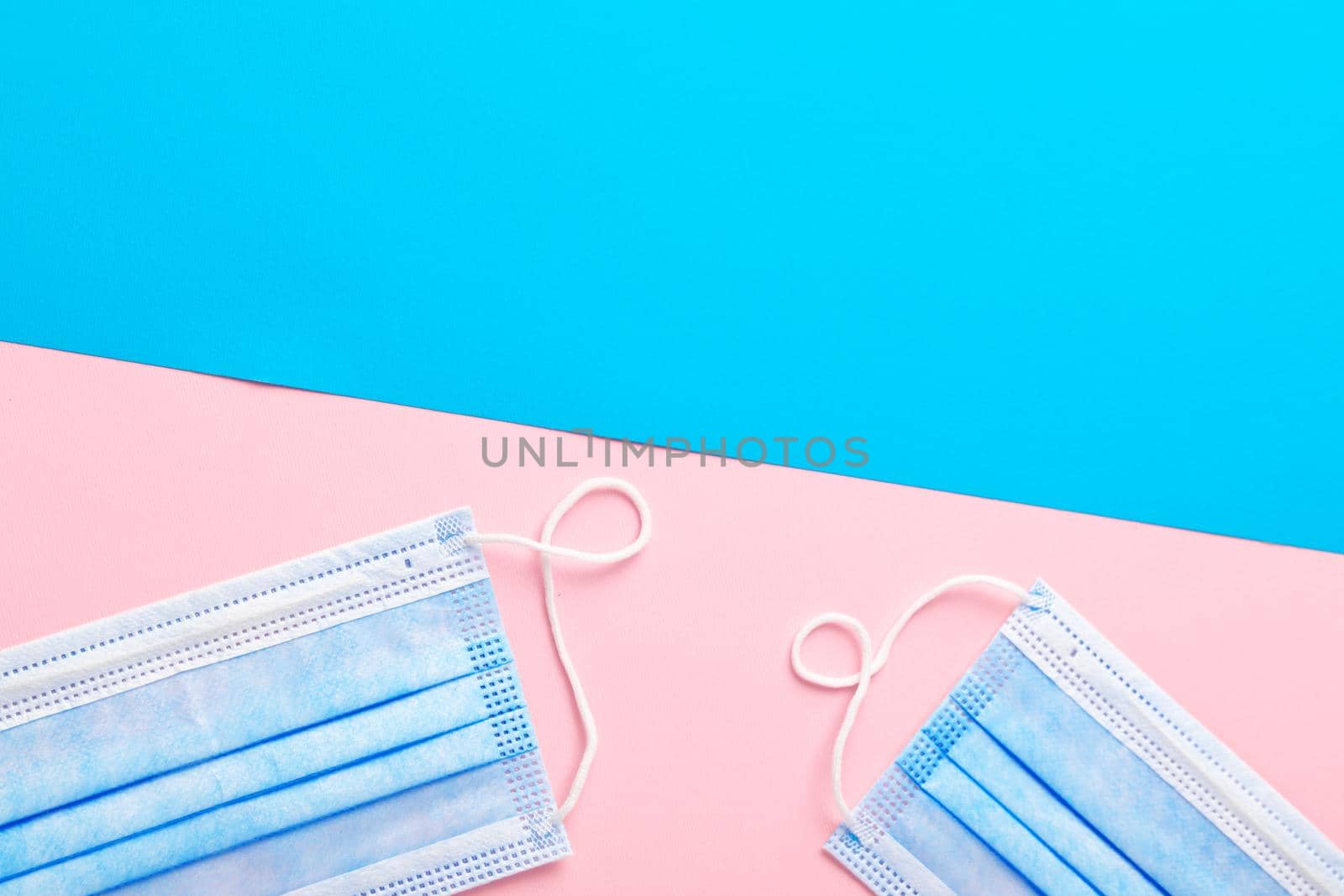 Medical face mask on pink and blue paper background with copy space top view