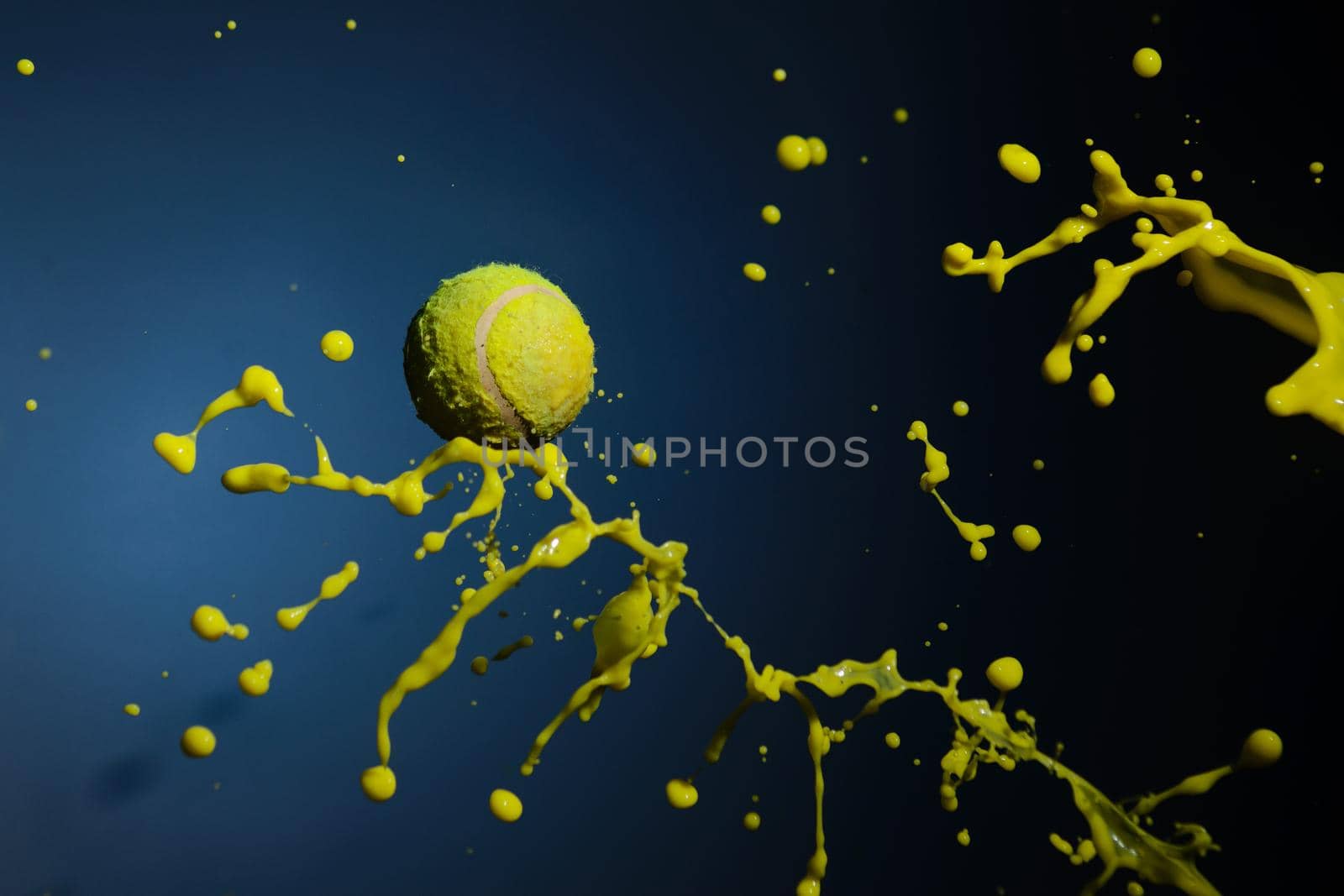 A tennis ball and splashes of yellow paint form a mantis figurine on a blue background.