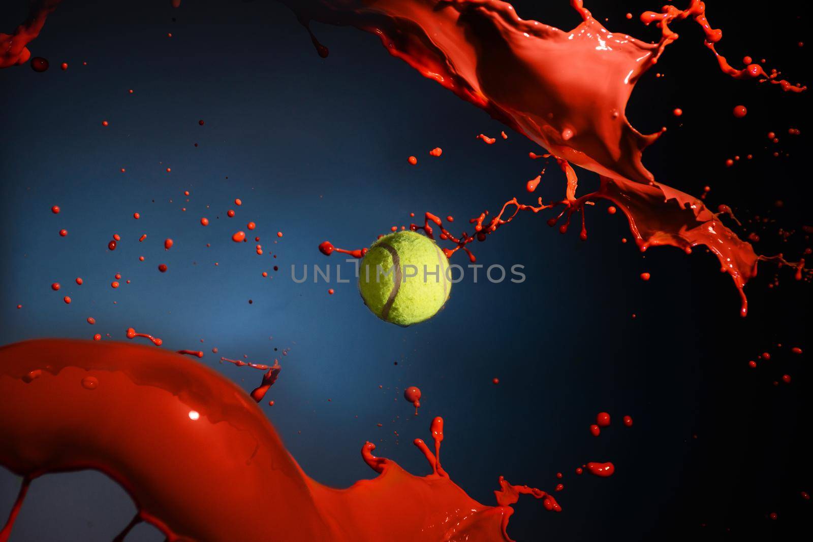 Isolated shot of red paint splash and tennis ball on blue background.