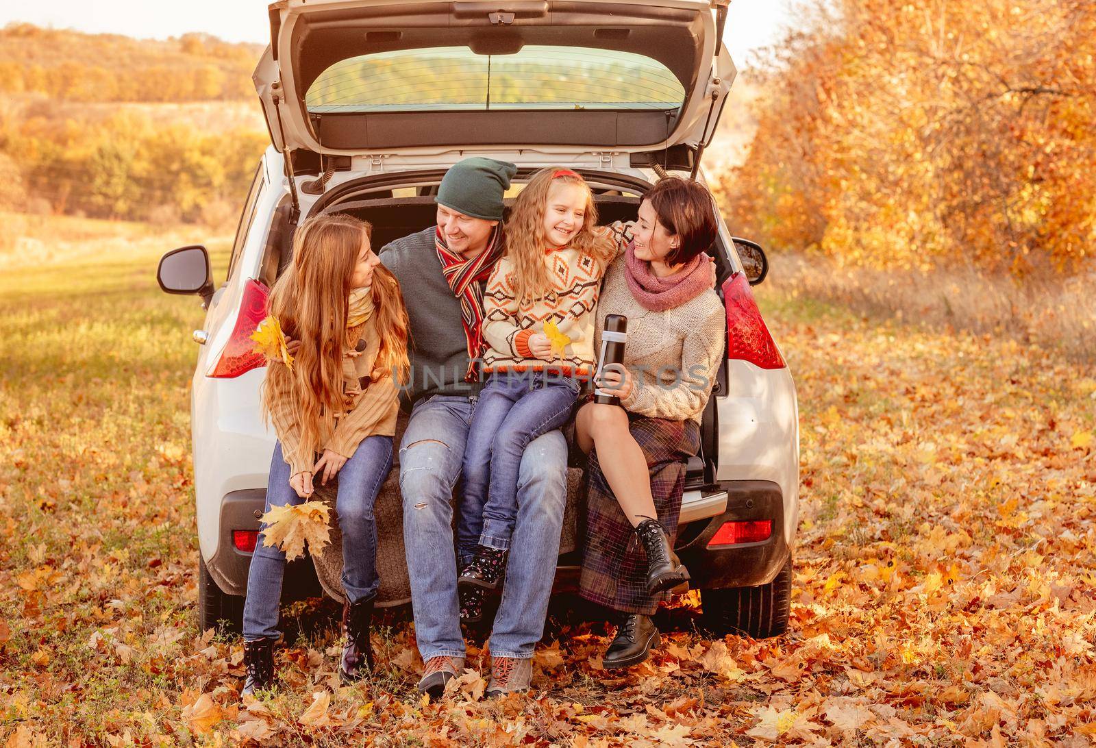 Happy family sitting in car trunk on autumn background