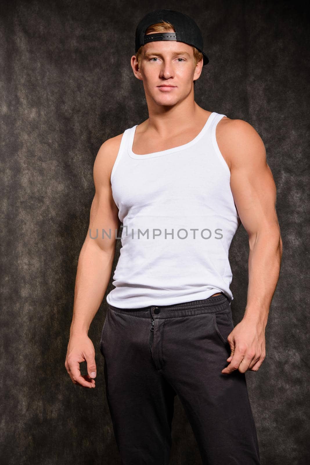 athletic guy in a vest and a baseball cap on black background