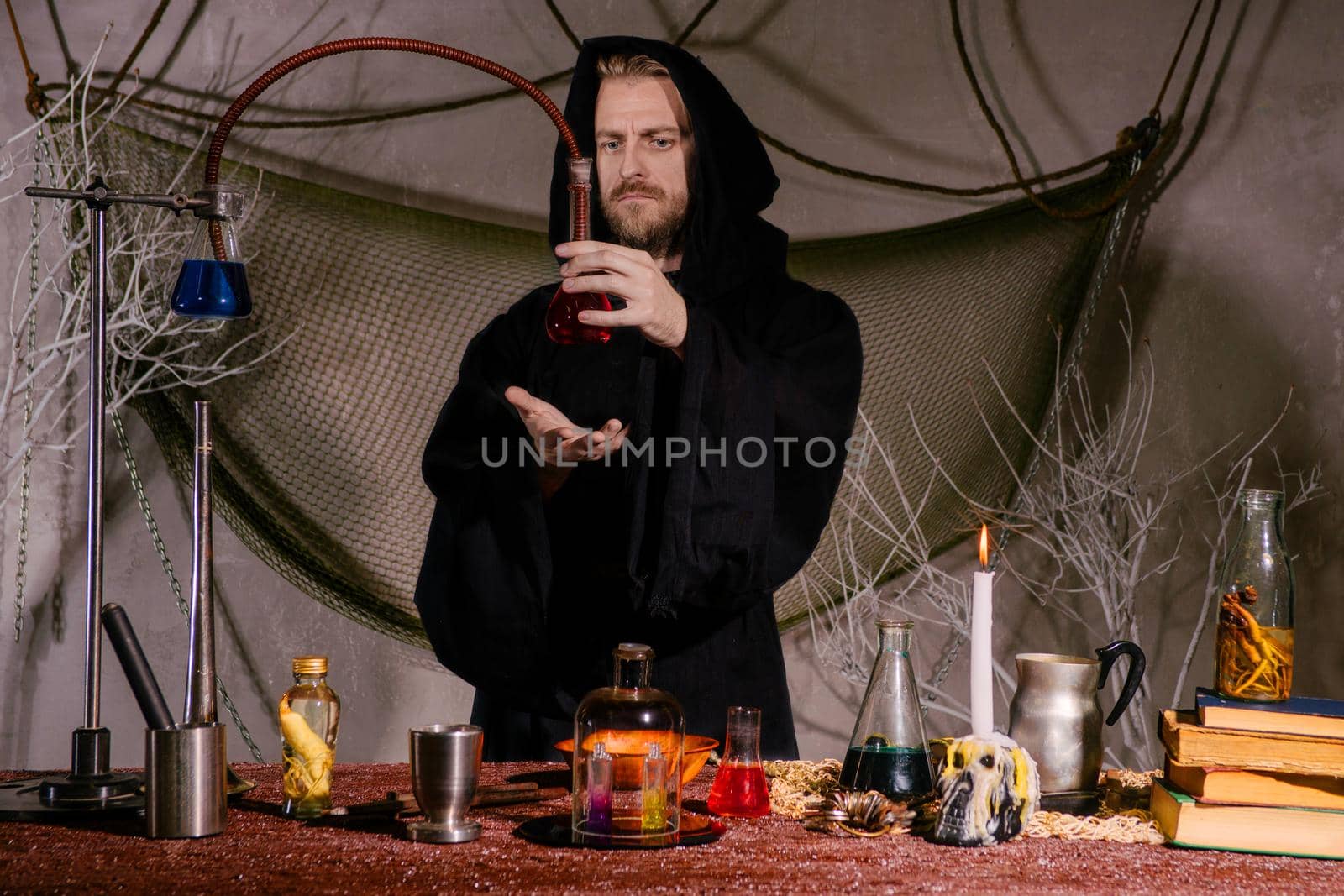 The medieval alchemist scientist conducts a ritual in his laboratory.. Halloween concept. The bearded magician in the mantle