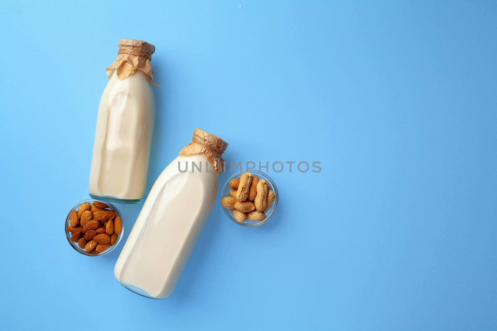 Bottles of vegan non dairy milk with various nuts on blue background, top view