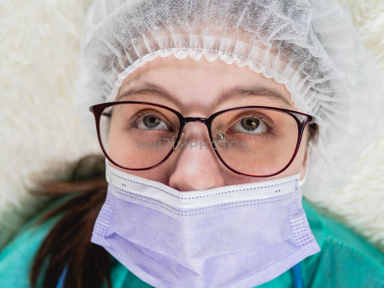 Young woman doctor nurse in surgical mask looks tired. Close-up, top view by Utlanov