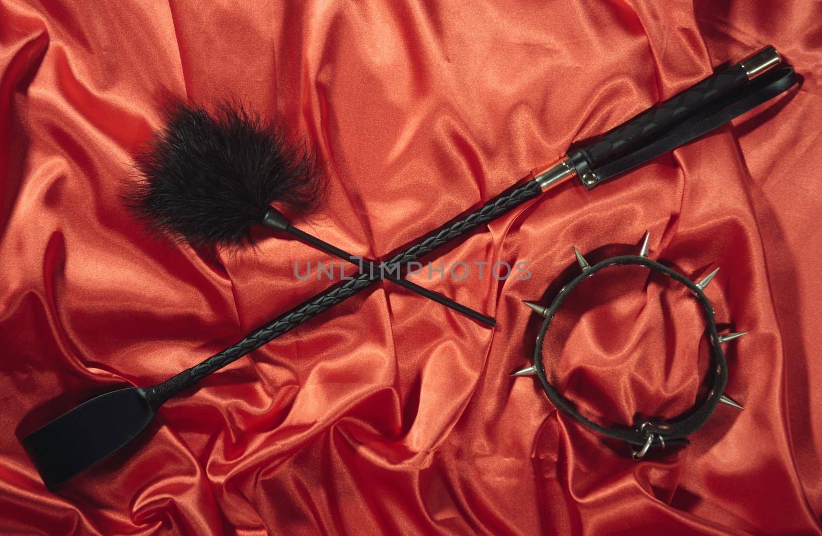 Bondage, kinky adult sex games, kink and BDSM lifestyle concept with a whip, feather stick, collar on red silk with copy space