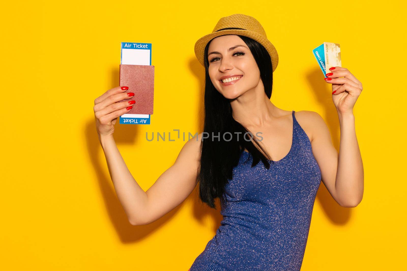 Young smiling excited woman student holding passport boarding pass ticket and credit card isolated on yellow background. Air travel flight - Image