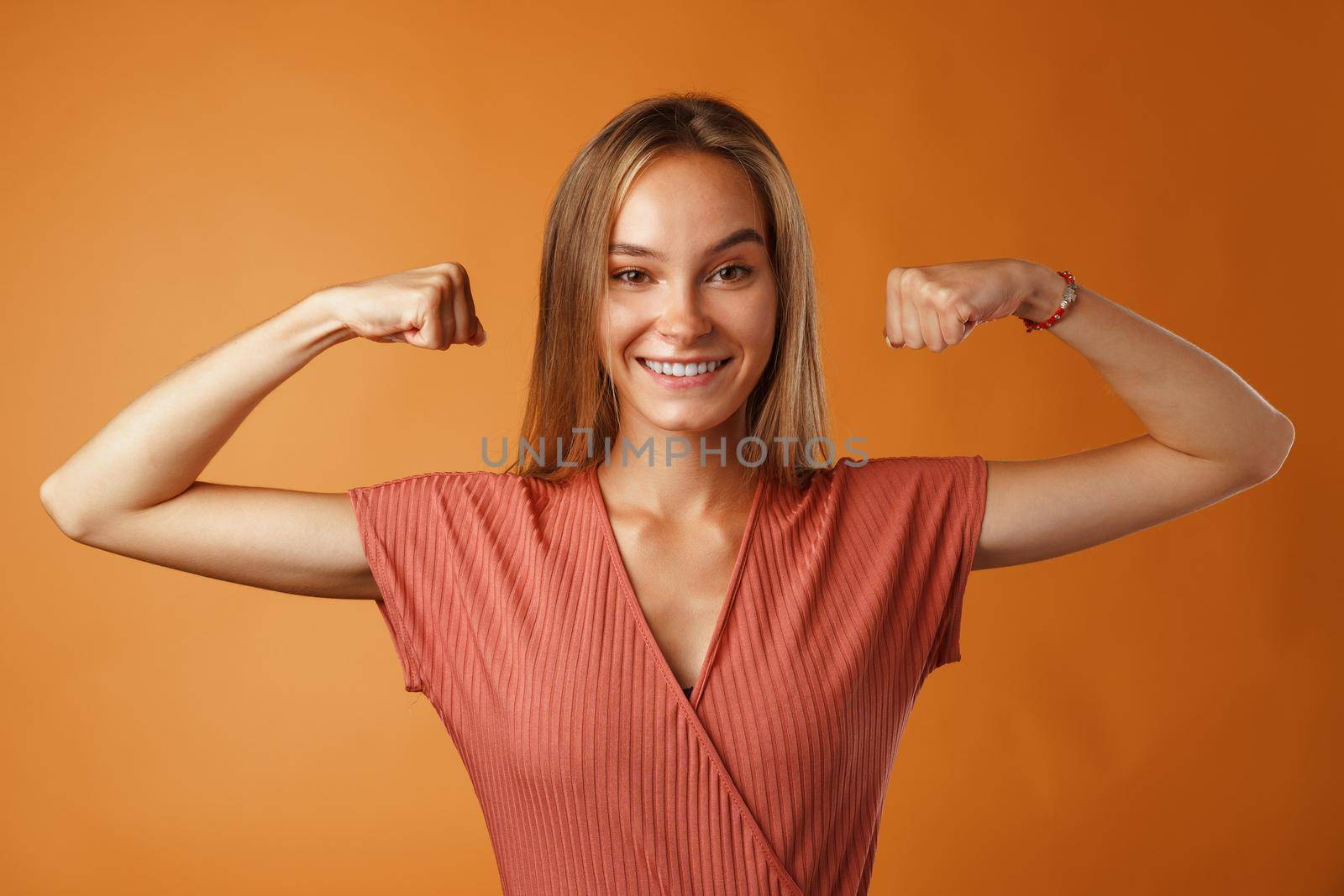 Funny young blonde woman showing how strong her hands are.against orange background