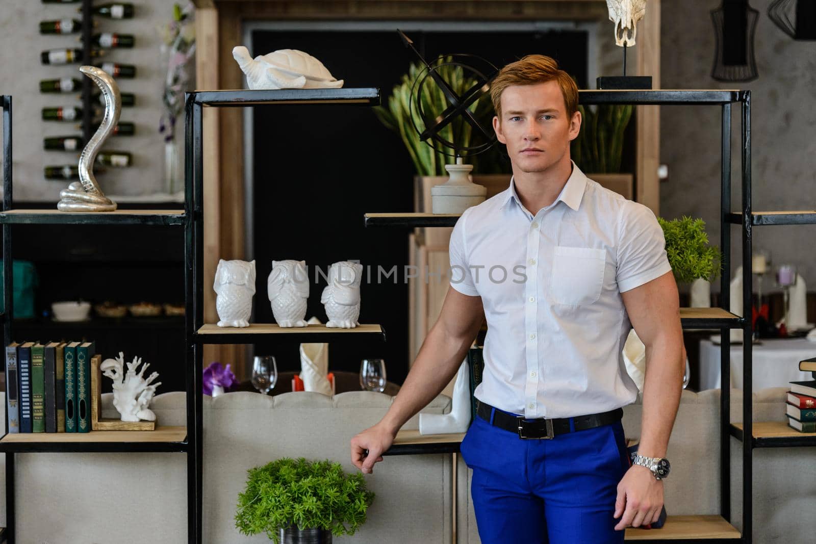 Young sporty man in white shirt and blue pants standing at home near books