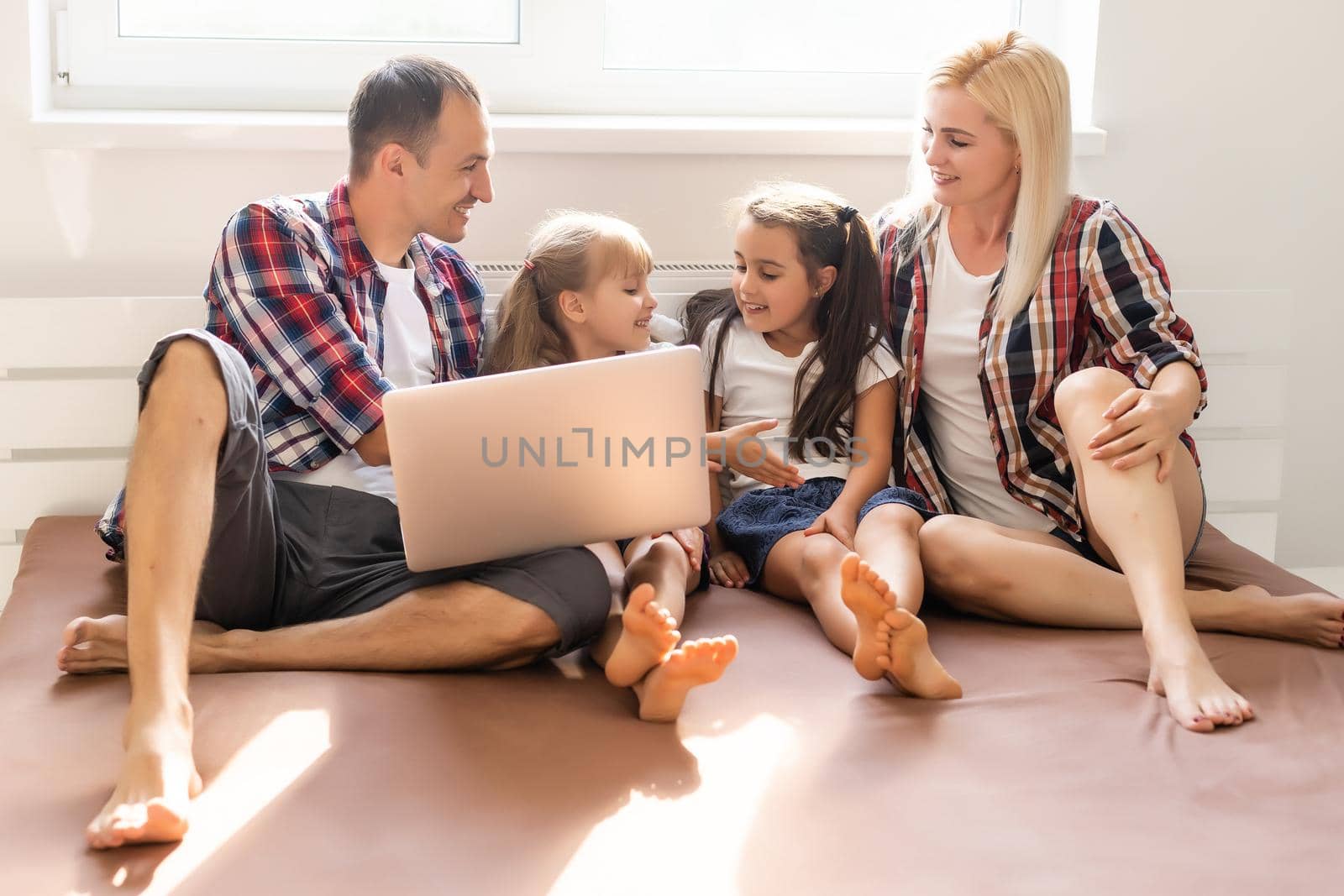 Happy family concept. Beautiful mother and handsome father with their daughters spending time together at home and lying on bed with laptop. by Andelov13