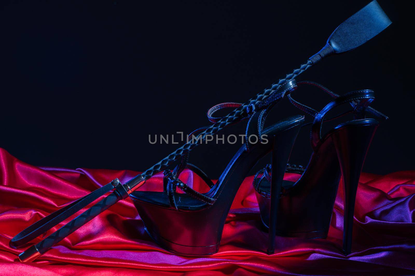 Adult sex games. Kinky lifestyle. Spank and a pair of black high-heeled shoes on the red linen. Bdsm outfit - Image