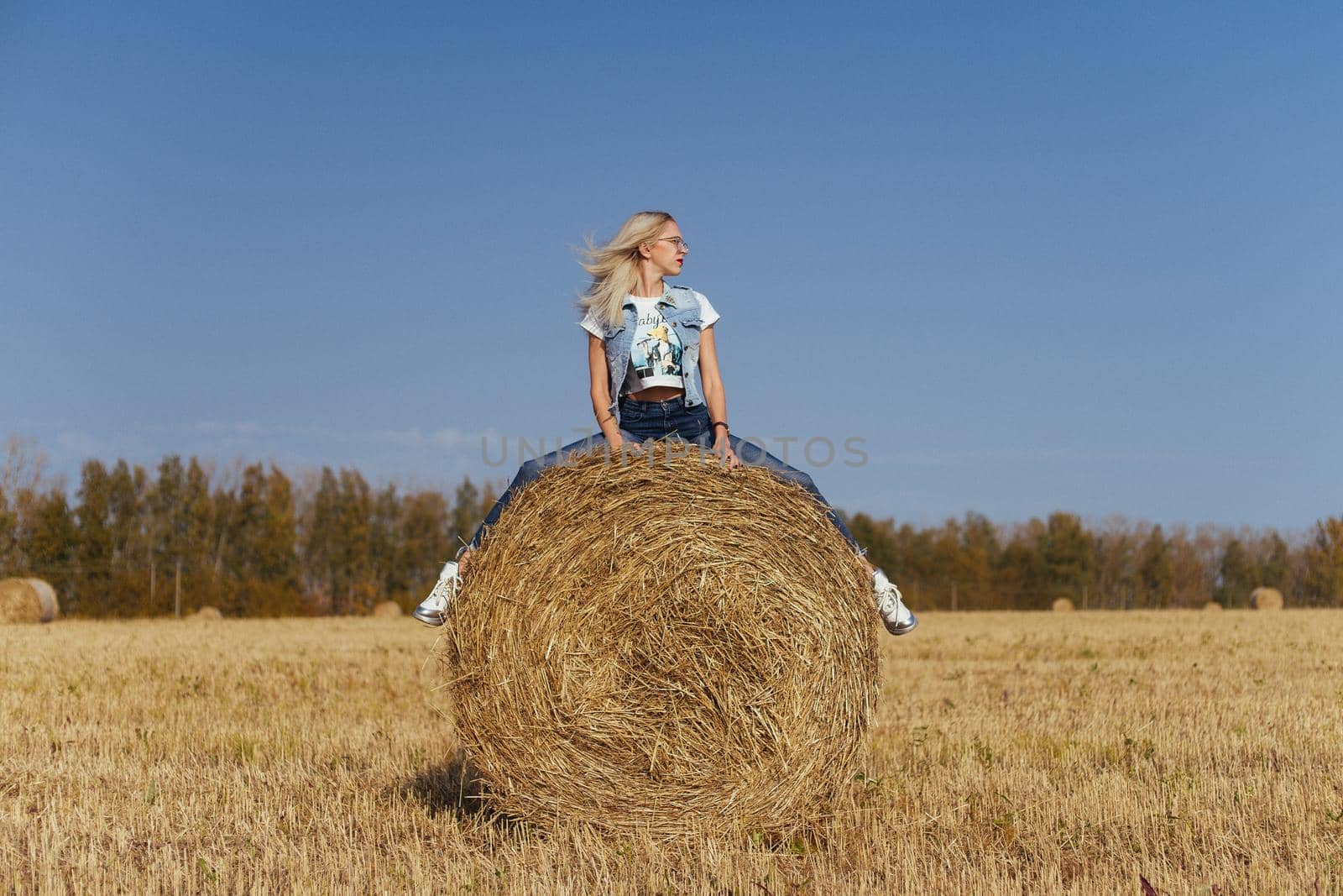 Beautiful girl villager posing in jeans on a bale of hay in a field