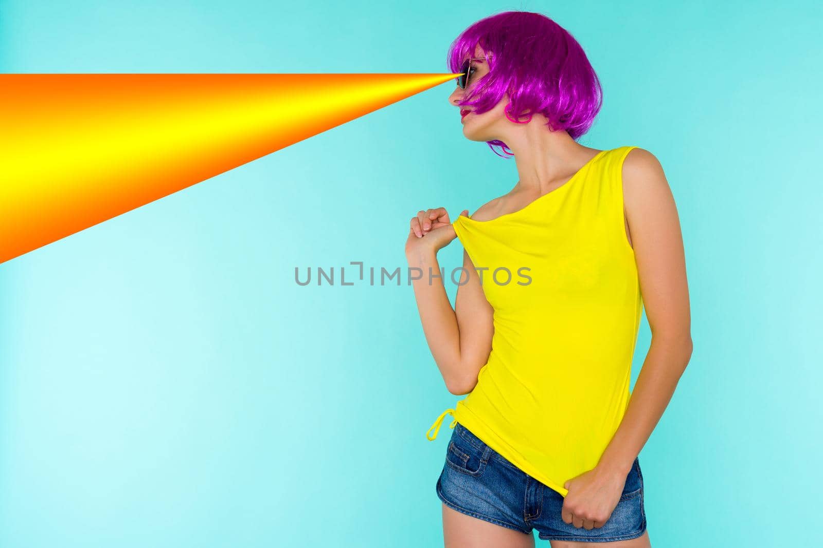 Portrait of young transgender woman in pink wig and sunglasses, yellow t-shirt shoots the orange laser out of his eyes on blue background - image