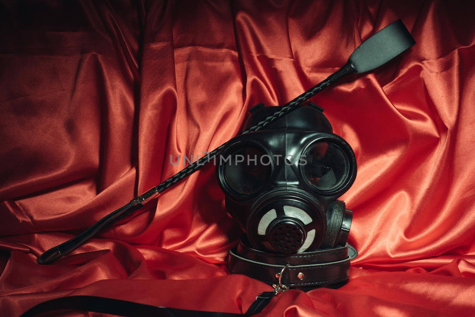 Close up bdsm outfit. Bondage, kinky adult sex games, kink and BDSM lifestyle concept with gas mask, whip, collar on red silk with copy space.