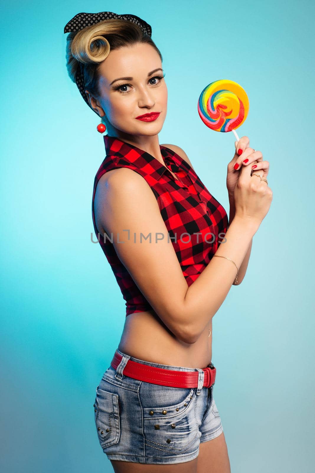 Portrait of beautiful woman with lollipop, dressed in pin-up style. Caucasian blond model posing in retro fashion and vintage concept studio shoot.