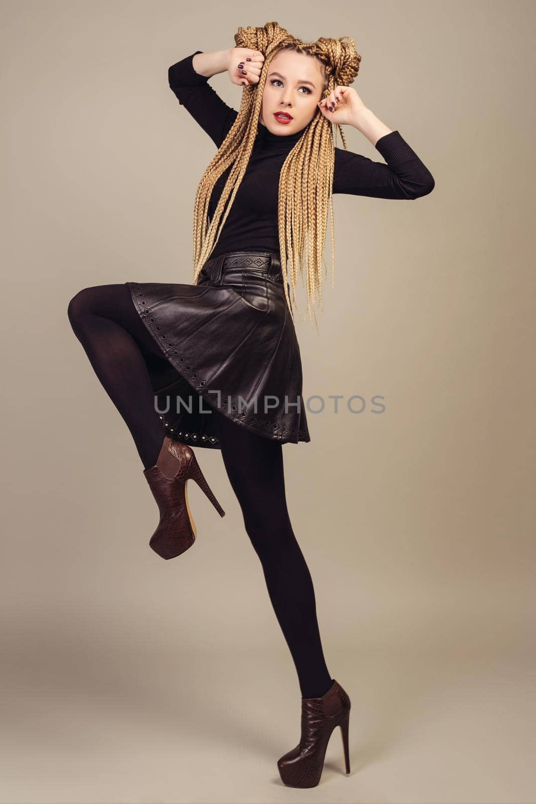 Portrait of a beautiful young girl with two ponytails,takes a step to the side raising his hands to his face. Isolated on gray background.