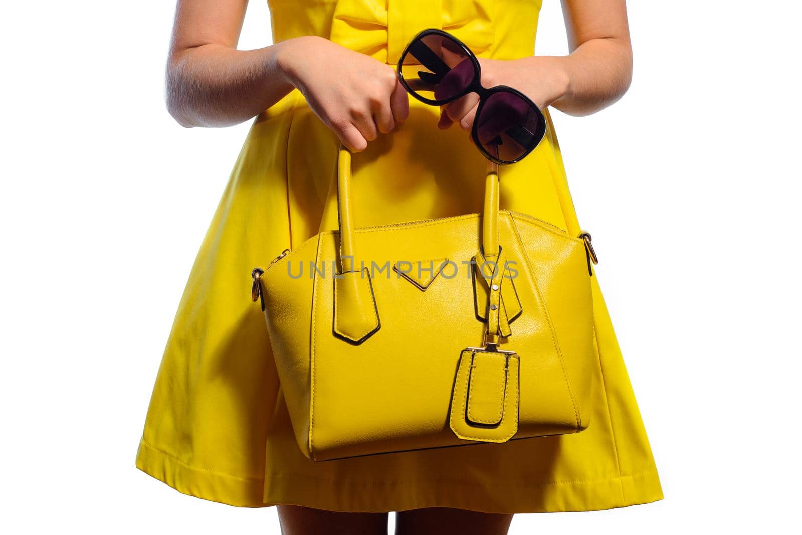 Elegant fashionable young woman in a yellow dress with a handbag and sunglasses in hand on a white background