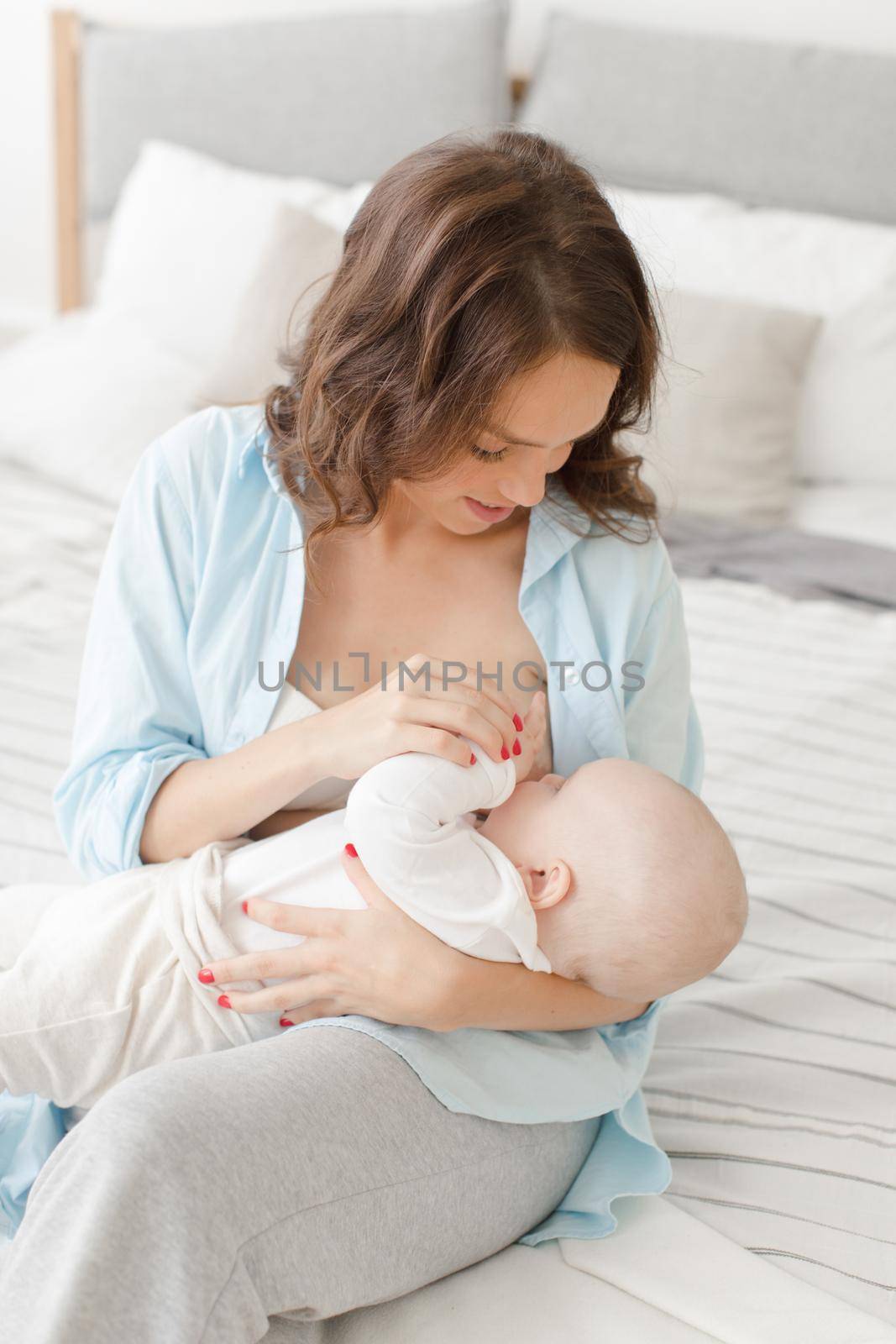 Happy young woman holding on hands her infant child. Mother breast feeding and hugging her baby boy