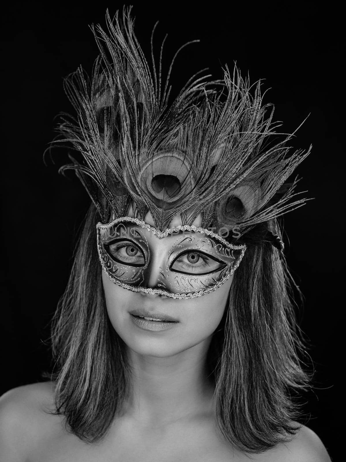 Black and white close-up portrait of a beautiful green-eyed woman in a Venetian carnival mask on a dark background. ring flash