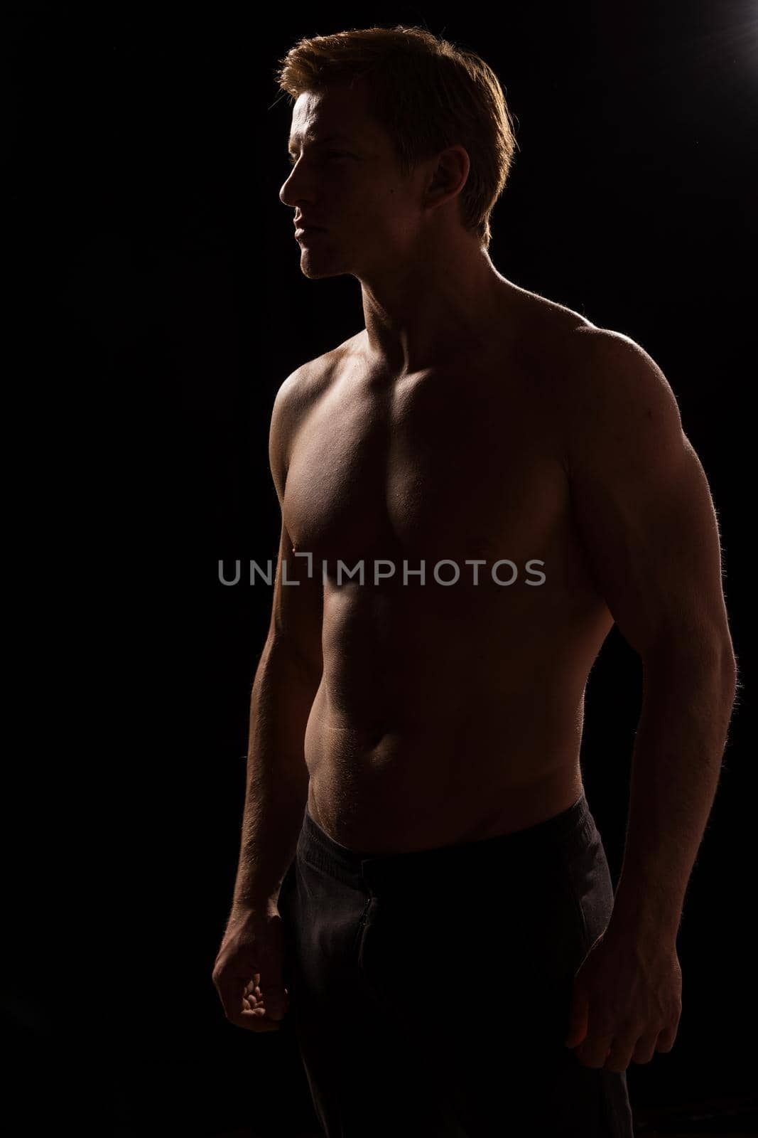 Male fitness model showing muscles in studio with a black background