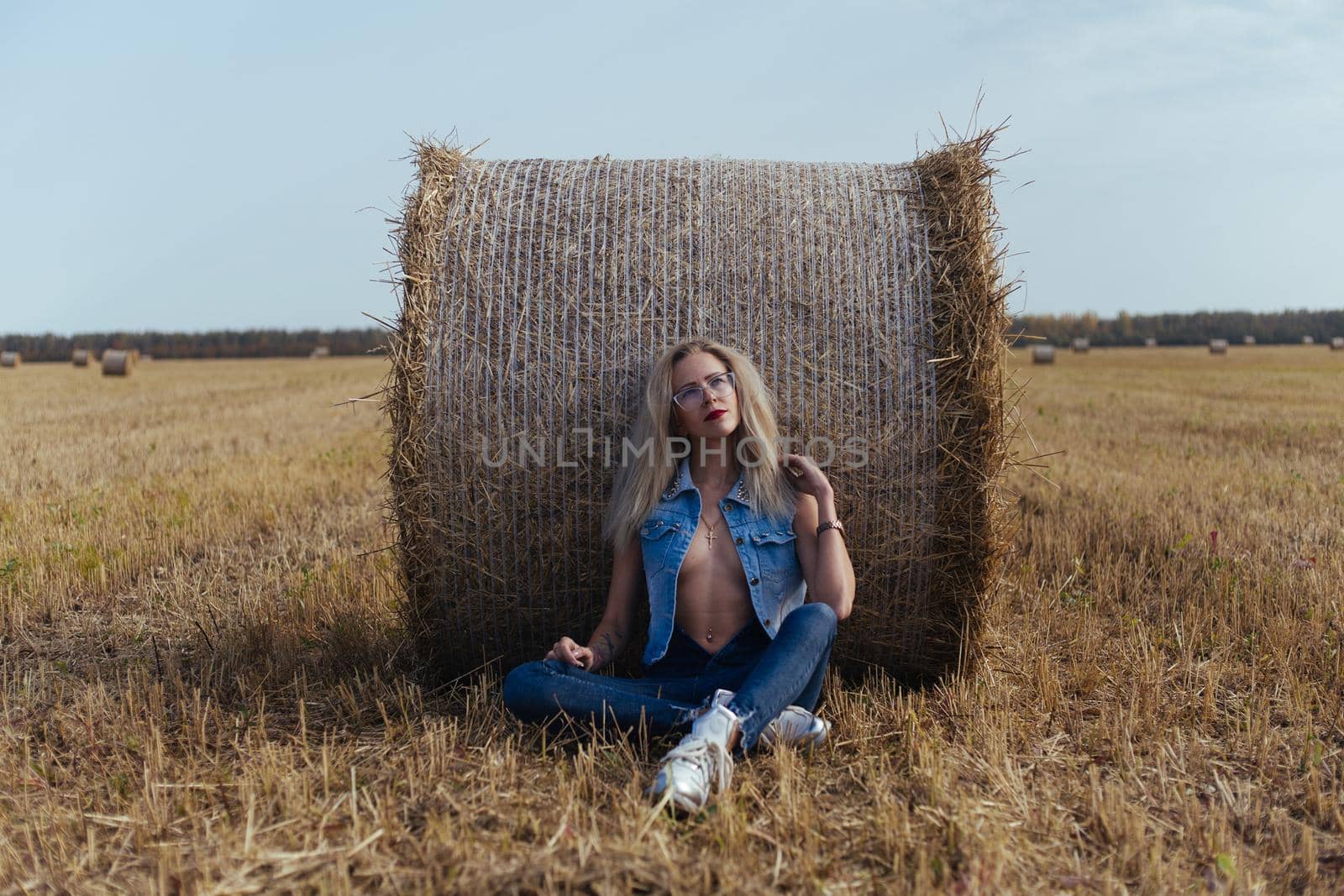 Beautiful girl villager posing in jeans near a bale of hay in a field