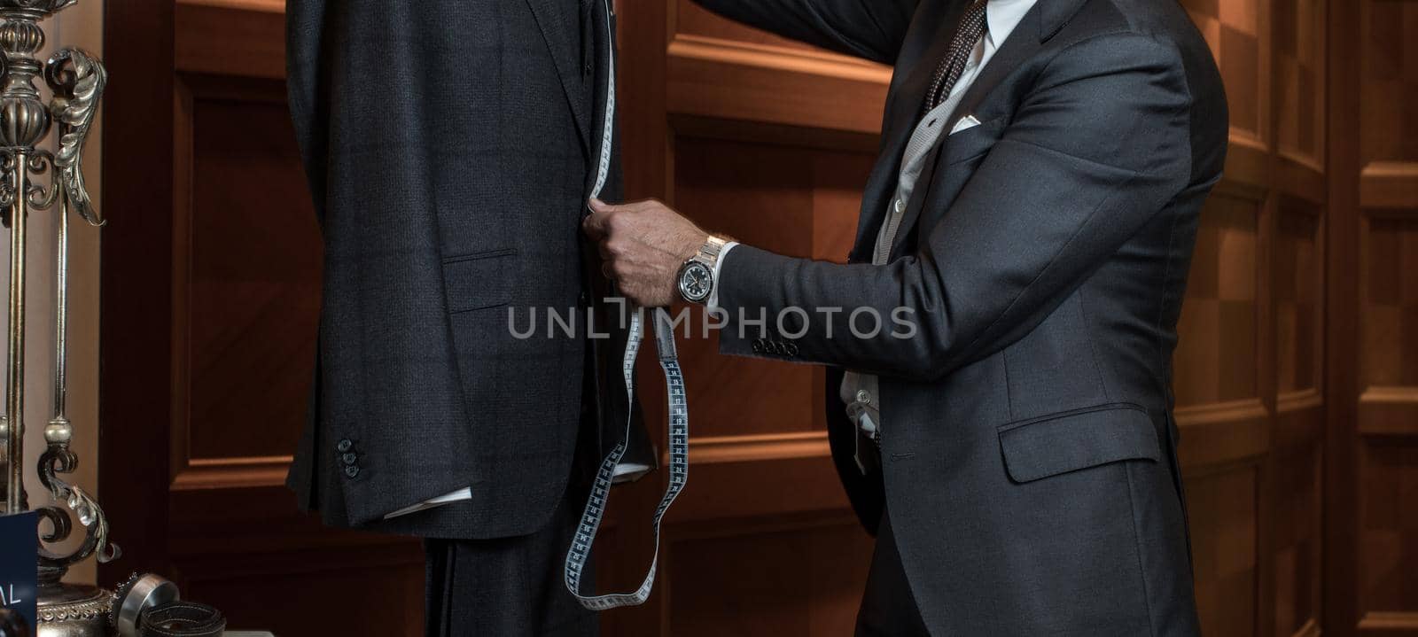 Unrecognizable tailor man measuring suit on dummy with tape-measure.