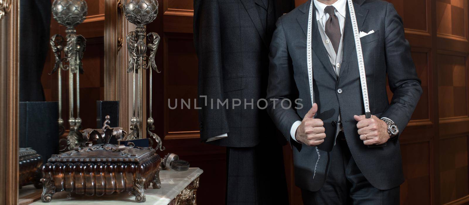 Man in suit in the interior of the boutique tailoring of individual suits. Hands of a tailor keep a tape centimeter to measure.