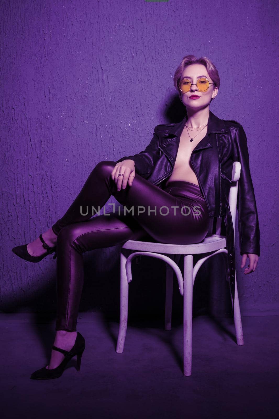A lonely young girl is sitting on a chair in the room. Illuminated by neon ultraviolet zine light.
