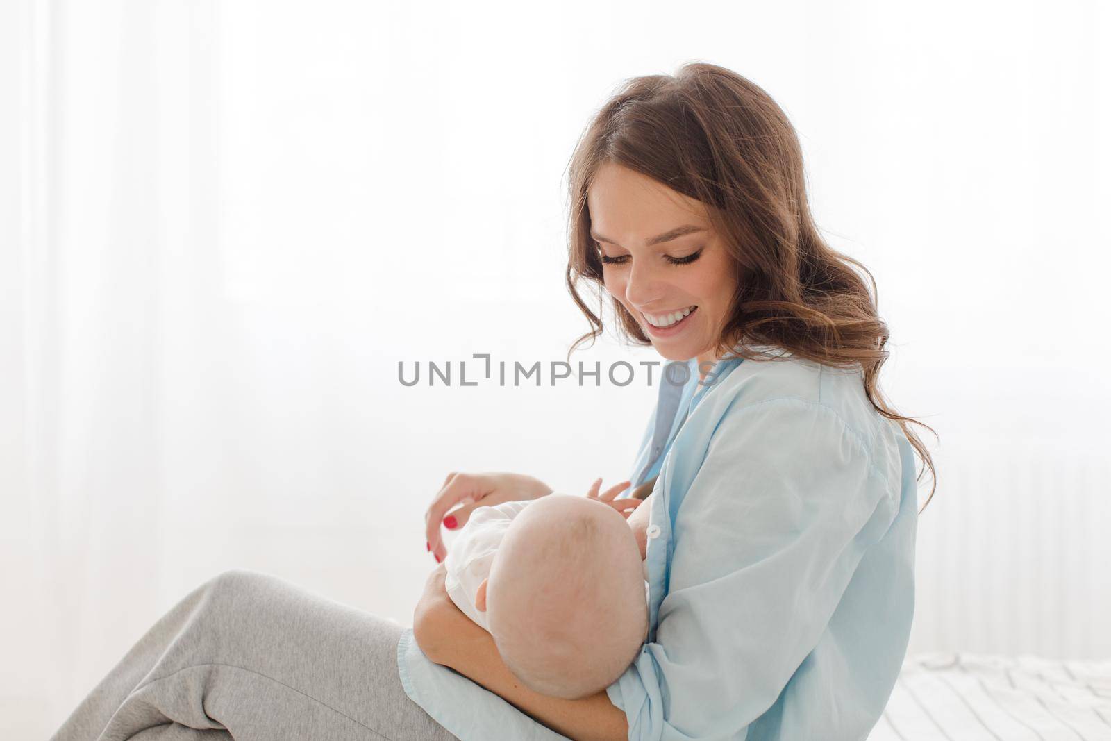 Happy young woman holding on hands her infant child. Mother breast feeding and hugging her baby boy